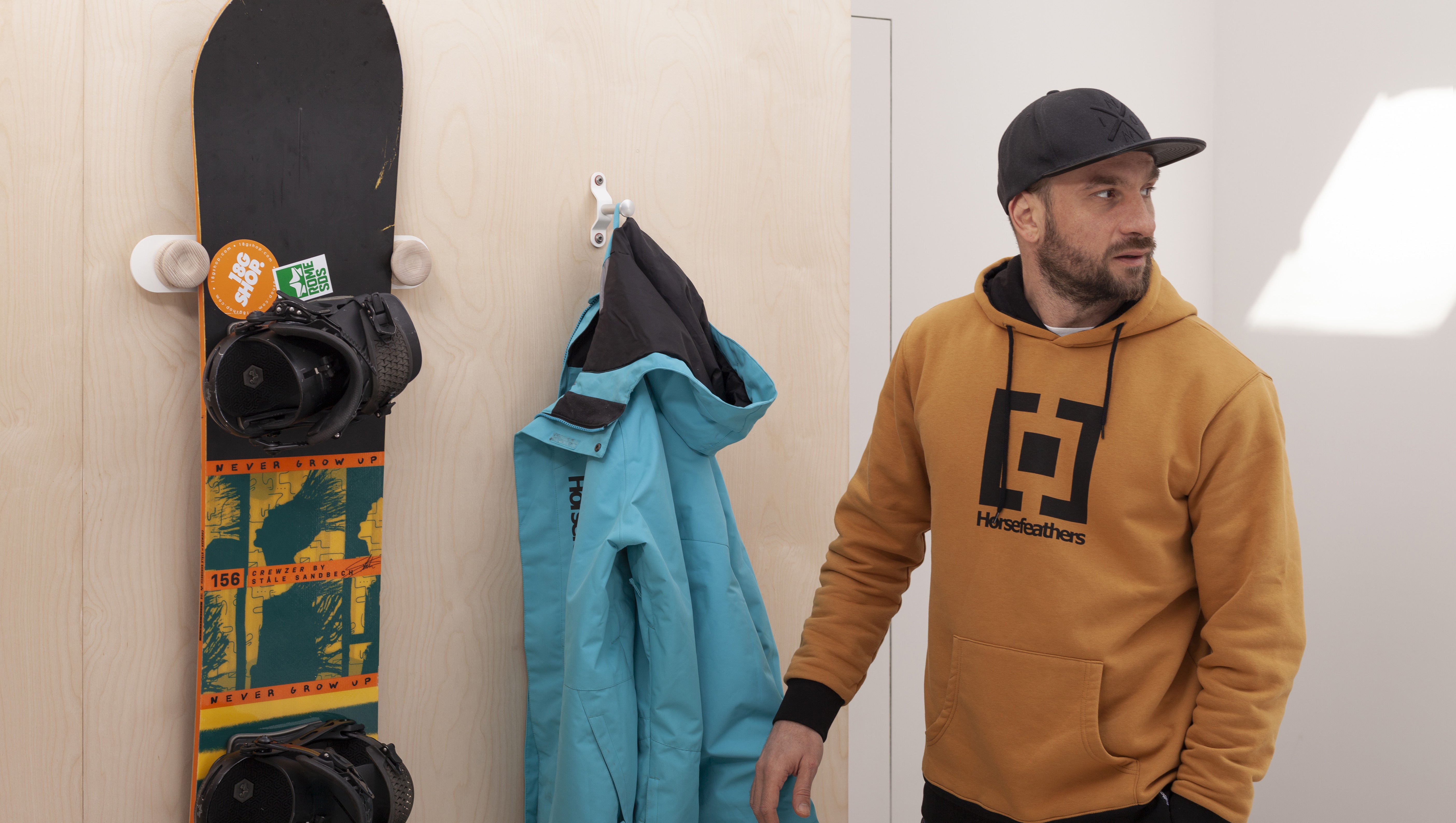 A snowboard and jacket neatly hung at home beside their owner